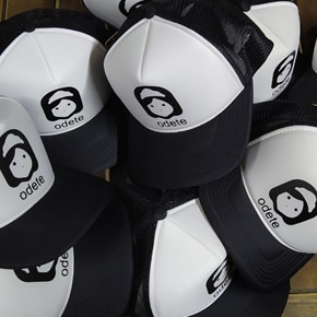 Boné Preto e Branco com a parte de trás e a aba em preto, a frente do boné em branco com a Logo da odete vetorizada em preto e abaixo da logo escrito odete em letra minúscula