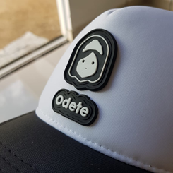 Boné Preto e Branco com a parte de trás e a aba em preto, a frente do boné em branco com a Logo da odete vetorizada em preto e abaixo da logo escrito odete em letra minúscula