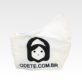Máscara Branca em algodão com a logo da odete na parte esquerda da bocheca na cor preta e abaixo da logo escrito odete.com.br em letra minúscula